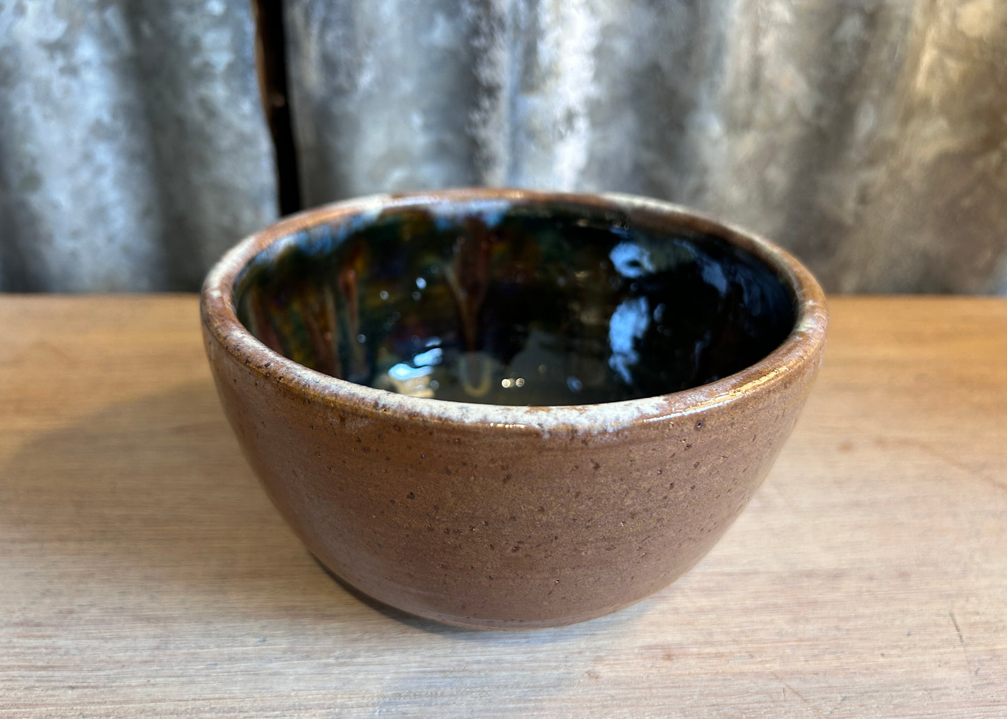 Ceramic bowl with brown exterior and black interior on a wooden surface