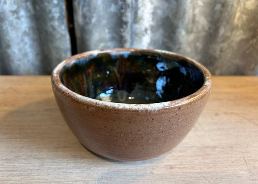 Ceramic bowl with brown exterior and black interior on a wooden surface