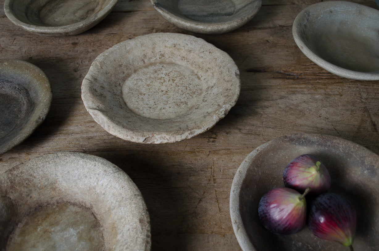 A collection of hand-carved Indian spice bowls made from Banswara marble, displayed on a wooden surface with some bowls containing fruit.